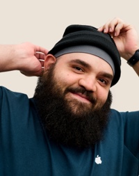 Portrait d’une personne de l’équipe de vente au détail d’Apple souriant; elle porte la barbe et un bonnet en tricot.