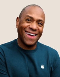 Portrait d’une personne de l’équipe de vente au détail d’Apple souriant; elle a des cheveux gris foncé courts.
