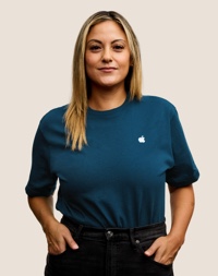 Portrait d’une personne de l’équipe de vente au détail d’Apple souriant; elle a de longs cheveux blond foncé.