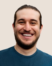 Portrait d’une personne de l’équipe de vente au détail d’Apple souriant; elle a les cheveux foncés et une barbe.