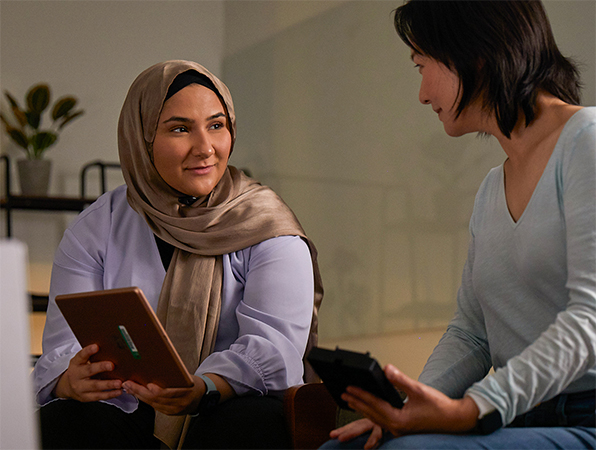سيدتان من أعضاء فريق التعلم الآلي والذكاء الاصطناعي في Apple تتعاونان معاً، تحمل إحداهما جهاز iPad والأخرى تحمل جهاز iPhone.